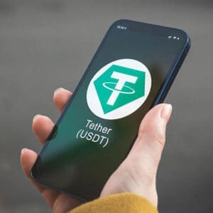 Tether USDT cryptocurrency symbol, logo. Business and financial concept. Hand with smartphone, screen with crypto icon closeup